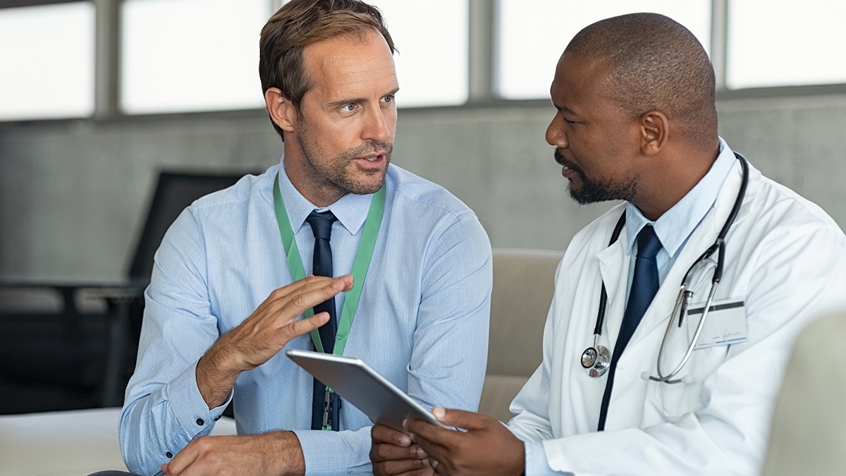 Doctor in conversation with pharmaceutical representative Pharmaceutical representative talking with doctor sitting on couch. African mature practitioner discussing results of the analysis with specialist while consulting diagnosis on digital tablet. Doctor in conversation with medical advisor in hospital room discussing patients report case.