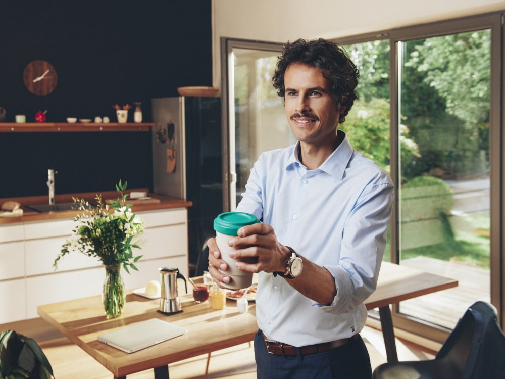 Egy férfi egy házban áll, és egy csésze kávét tart