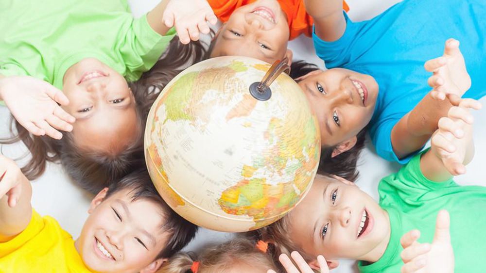 Mosolygó gyerekek feküdnek a földön egy földgömb körül, miközben felnyújtják a karjukat.