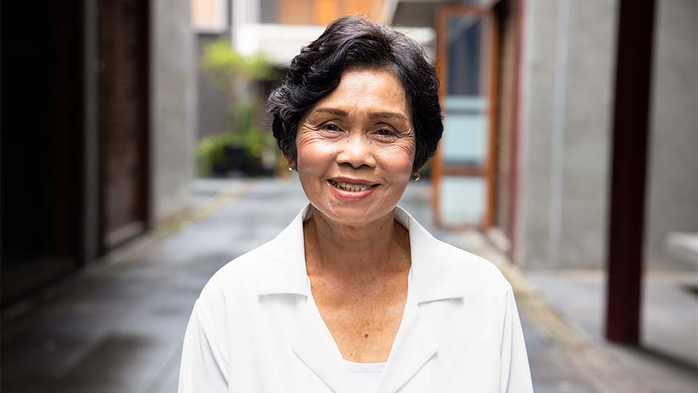 Egy idős nő meleg mosolyral áll egy bájos utcában. 